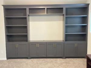 Built-in entertainment center painted dark gray with shelving, closed cabinets, and brass pull hardware