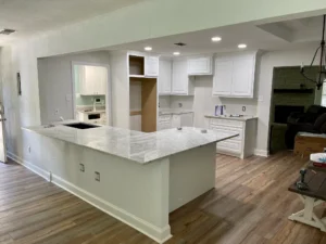 Kitchen under renovation with white cabinets, a large U-shaped granite countertopisland, and wood-look flooring