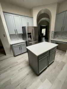 Modern kitchen with light gray shaker cabinets, a central island, and wood-look luxury vinyl flooring