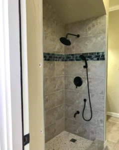 Walk-in shower with large beige tiles, a decorative glass mosaic accent stripe, and matte black fixtures