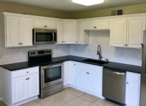 White kitchen cabinets with black countertops, stainless steel appliances, and white subway tile backsplash