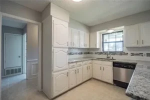 White kitchen cabinets with raised panel doors, stainless steel dishwasher, and a grey and white backsplash